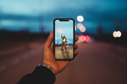 Junger Mann fotografiert Frau auf Skateboard in der Abenddämmerung - RSGF00627