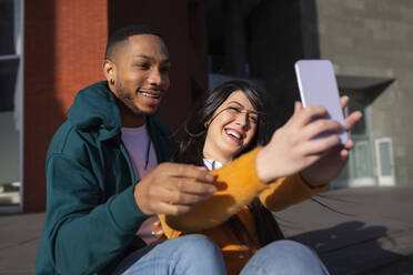 Fröhliche Frau mit Freund nimmt Selfie durch Handy - MTBF00908