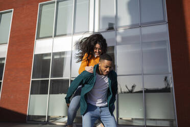 Man giving piggyback to girlfriend against glass building - MTBF00910