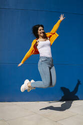 Fröhliche junge Frau mit ausgestreckten Armen, die auf dem Fußweg hochspringt - MTBF00926