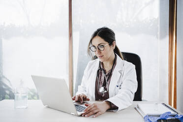 Weibliches medizinisches Fachwissen bei der Benutzung eines Laptops, während sie im Krankenhaus am Fenster sitzt - EBBF02660