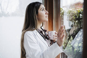 Nachdenkliche Ärztin schaut beim Kaffee durch das Fenster - EBBF02680