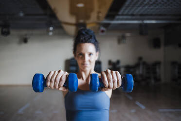 Weibliche Sportlerin hält Hanteln im Fitnessstudio - EBBF02695