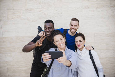 Glückliche Sportler, die ein Selfie mit ihrem Smartphone vor einer Wand machen - EBBF02699