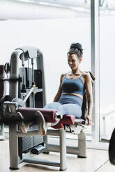 Lächelnde Sportlerin, die im Fitnessstudio an einer Gewichthebevorrichtung trainiert - EBBF02714