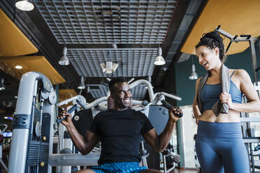 Männliche und weibliche Sportler lächelnd, während sie sich im Fitnessstudio anschauen - EBBF02724