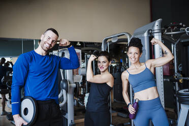 Smiling sports people flexing muscles while standing in health club - EBBF02730