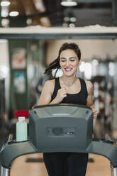 Happy sportswoman exercising on treadmill in gym - EBBF02734