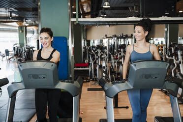 Smiling female athletes exercising on treadmill in health club - EBBF02738