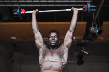 Selbstbewusster muskulöser Sportler beim Training mit einer Langhantel im Fitnessstudio - EBBF02762