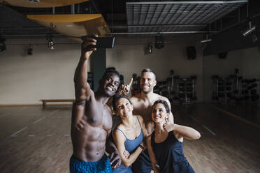 Smiling male and female sports people taking selfie through smart phone in gym - EBBF02785