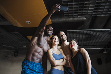 Lächelnde männliche und weibliche Athleten, die ein Selfie über ein Smartphone im Fitnessstudio machen - EBBF02786