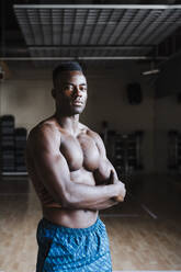 Shirtless sportsman with arms crossed standing in gym - EBBF02789