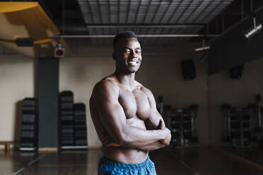 Smiling male athlete standing with arms crossed in health club - EBBF02790