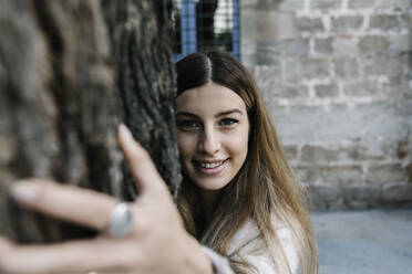 Young woman smiling while hugging tree - XLGF01305