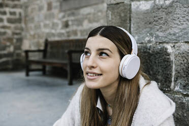 Lächelnde Frau mit Kopfhörern an einer Steinmauer - XLGF01307