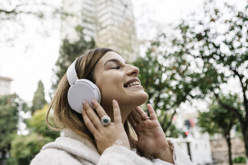 Happy young woman listening music on headphones outdoors - XLGF01310