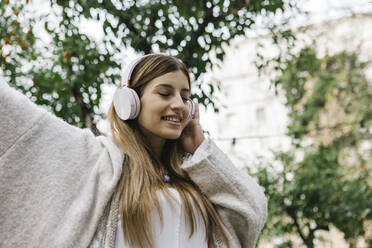 Glückliche Frau hört Musik über Kopfhörer im Freien - XLGF01311