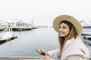 Smiling woman with mobile phone at the waterfront - XLGF01314