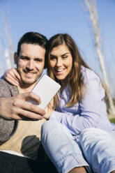 Boyfriend taking selfie through mobile phone with girlfriend at park - ABZF03482