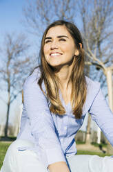 Lächelnde Frau, die wegschaut, während sie im Park sitzt - ABZF03488