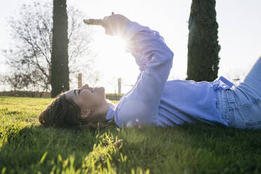 Smiling mid adult woman using mobile phone while lying on grass - ABZF03490