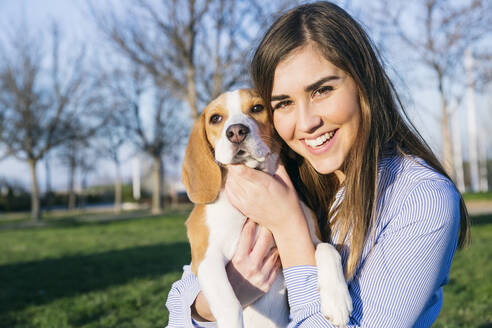 Female pet owner smiling while embracing dog at park - ABZF03501