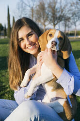 Mid adult woman sitting with dog at park during sunset - ABZF03502