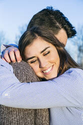 Smiling girlfriend embracing boyfriend during sunset - ABZF03506