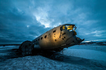 Teil eines riesigen abgestürzten Flugzeugs in einem gefrorenen See vor einem dunklen, bewölkten Himmel in Island - ADSF21437