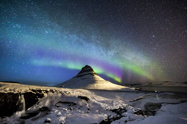 Erstaunlicher Anblick des Polarlichts, das am Nachthimmel mit Sternen über einem schneebedeckten Berg im Winter in Island leuchtet - ADSF21440