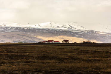 Landschaftliche Ansicht von Landhäusern in einem Trockental vor dem Hintergrund verschneiter Berge im Winter in Island - ADSF21443