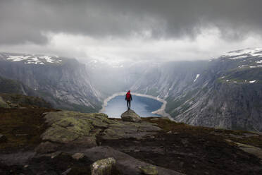 Rückansicht eines Forschers, der an einem bewölkten Tag während eines Urlaubs in Norwegen am Rande der Felsformation Trolltunga steht - ADSF21449