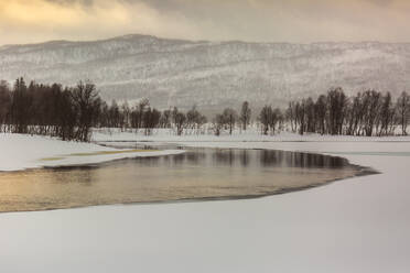 Landschaft eines nicht zugefrorenen Sees vor dem Hintergrund verschneiter Berge im Winter in Norwegen - ADSF21459