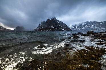 Erstaunliche Meereslandschaft mit felsiger Küste und rauen Bergen mit Schnee bedeckt im Winter in Norwegen auf bewölktem Tag - ADSF21463