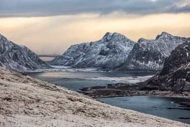 Malerische Landschaft von felsigen Bergen mit Schnee bedeckt in der Nähe von Meer unter Sonnenuntergang Himmel in Norwegen im Winter - ADSF21466