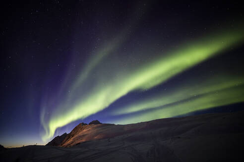 Niedriger Winkel des spektakulären nächtlichen Sternenhimmels mit leuchtenden violetten und grünen Polarlichtern über schneebedeckten Bergen im Winter in Norwegen - ADSF21472