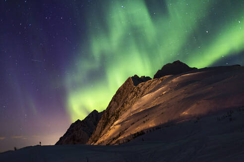 Niedriger Winkel des spektakulären nächtlichen Sternenhimmels mit leuchtenden violetten und grünen Polarlichtern über schneebedeckten Bergen im Winter in Norwegen - ADSF21474