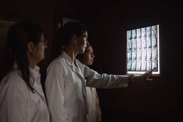 Eine Gruppe von Ärztinnen sieht sich in einem dunklen Raum bei ausgeschaltetem Licht ein Röntgenbild an, und eine zeigt darauf - ADSF21499