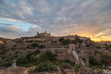 Aerial view of old city with historic buildings and stone castle on hill against cloudy sky during sunset in Toledo, Spain - ADSF21521