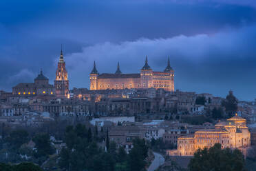 Luftaufnahme der Altstadt mit historischen Gebäuden und einer Steinburg auf einem Hügel bei bewölktem Himmel während des Sonnenuntergangs in Toledo, Spanien - ADSF21524