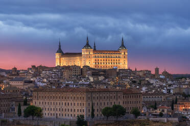 Luftaufnahme der Altstadt mit historischen Gebäuden und einer Steinburg auf einem Hügel bei bewölktem Himmel während des Sonnenuntergangs in Toledo, Spanien - ADSF21526