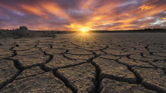 From above of drought cracked lifeless ground under colorful cloudy sky at sunset time - ADSF21530