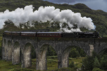 Altmodischer Dampfzug auf dem Glenfinnan-Viadukt in den Bergen an einem bewölkten Tag in Schottland - ADSF21541