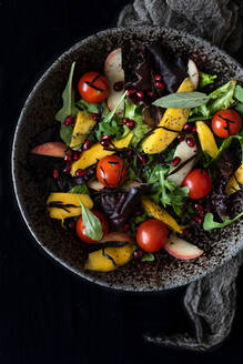 Draufsicht auf einen leckeren, nahrhaften Salat mit verschiedenen reifen Zutaten in einer Schüssel auf schwarzem Hintergrund - ADSF21556