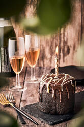 Köstlicher Schokoladenkuchen mit brennender Kerze, serviert auf einer Schiefertafel auf einem Tisch mit Gläsern Champagner im Cafe - ADSF21580