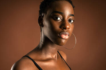 Slender black woman with short hair standing against brown background looking at camera - ADSF21616