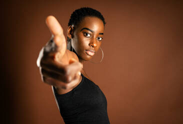 African American female with trendy earrings pointing at looking at camera against brown background - ADSF21620