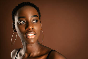 Slender black woman with short hair standing against brown background - ADSF21622