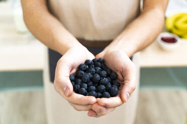 Man holding fresh blueberries in kitchen - GIOF11745